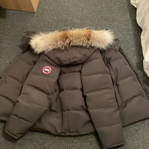 Grå dunjacka från Canada Goose - Säljer en grå dunjacka från Canada Goose i mycket bra skick. Jackan har en fluffig pälsfodrad huva och är perfekt för kalla vinterdagar. Den har långa ärmar . Märkets logga syns tydligt på ärmen. Supervarm och stilren!  Pris kan diskuteras. Hallands län/skåne