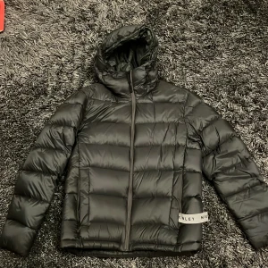 Mörkgrön pufferjacka från McKinley - Snygg grön pufferjacka från McKinley med huva och dragkedja. Perfekt för kyliga dagar med sin quiltade design som håller värmen. Jackan har en stilren look och är idealisk för både stad och natur.