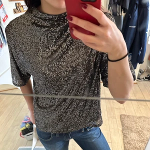 Glittrig topp från H&M - Säljer en glittrig topp från H&M i storlek L. Toppen har en lös passform med trekvartsärmar och är perfekt för festliga tillfällen. Den är täckt av silverglitter som ger en snygg och iögonfallande look. Perfekt för att lysa upp vilken outfit som helst! HELT PERFEKT FÖR NYÅR! 