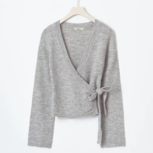 Grå omlottkofta från Gina Tricot - Säljer en mysig grå omlottkofta från Gina Tricot i storlek XS. Koftan har långa ärmar och en knytning i sidan för en stilren look. Perfekt för kyligare dagar. Priset går absolut att diskuteras.