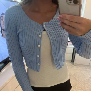 Ljusblå kofta med pärlknappr - Fin ljusblå kofta med pärlknappar från Monki i storlek S, som man kan ha både knäppt och uppknäppt, utan eller med linne.