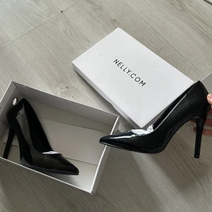 Svarta pumps från Nelly - Säljer ett par eleganta svarta pumps från Nelly. De har en spetsig tå och hög klack, perfekt för festliga tillfällen. Skorna är i nyskick och kommer i originalförpackning.