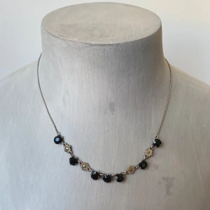 Elegant halsband med svarta pärlor - Säljer ett vintage halsband med svarta pärlor och detaljer i silver. Perfekt för en festlig kväll eller en elegant middag. Kedjan är tunn och smidig, vilket gör att pärlorna verkligen står ut. Detaljerna mellan pärlorna ger en touch som är både unik och stilren. Okänt material. 44 cm långt 