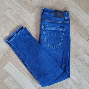 Mörkblå jeans från Signal - Ett par mörkblå jeans från Signal. 98,5% bomull och 1,5% elastan. Fickor fram och bak. Knäppning på framsidan med dragskedja och knapp. Välanvända, men fint skick och av bra kvalitet. Blivit blekta vid höger ficka, vilket syns på bild 2. 