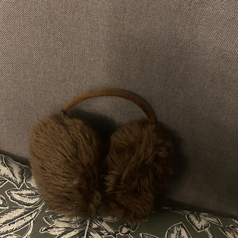 Snygga och varma bruna öronmuffar i pälsmaterial. Perfekta för att hålla öronen varma under kalla dagar. De har en enkel design med ett matchande brunt band.. Asusteet.
