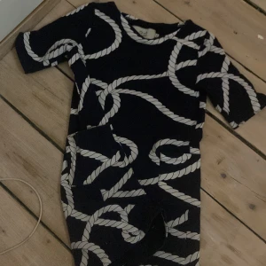 Svart klänning med repmönster - Snygg svart klänning med ett unikt repmönster i vitt. Klänningen har korta ärmar och en kroppsnära passform som ger en stilren look. Perfekt för dig som vill sticka ut med ett annorlunda mönster.