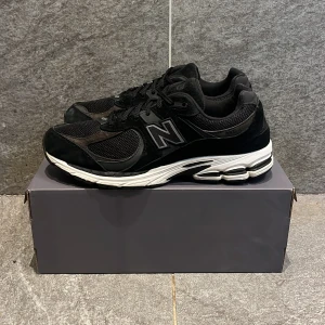 New Balance 2002r - Snygga svarta sneakers från New Balance i svart mocka och vit sula. Skorna är väldigt sköna och är i bra material, skorna är i bra skick det ända som är teken på andvändning är att mockan är gråare på vissa ställen som toeboxen men det är vanligt. Skorna är i storlek 45,5 men är lite små i storleken, har orginal box. Skriv vid mer frågor.