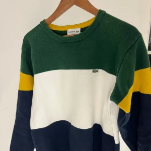 Flerfärgad tröja från Lacoste - Säljer en snygg flerfärgad tröja från Lacoste i grönt, vitt, gult och blått. Den är i bra skick och gjord i redigt och skönt tyg. Tröjan är i US size 5 vilket innebär att den ligger precis mellan Small och Medium. Den är lite för liten för mig som normalt bär medium och är 180 samt väger 75kg.