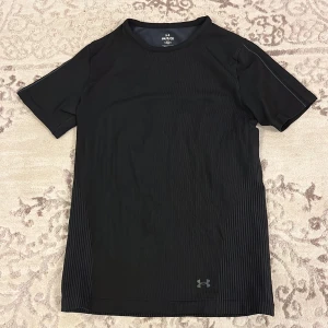 Svart t-shirt från Under Armour - Snygg svart t-shirt från Under Armour med diskret randigt mönster på sidorna. Perfekt för träning med sin tighta passform och korta ärmar. En del av deras RUSH-kollektion. Tröjan är endast använd två gånger och lapparna är avklippta då de störde. Köpt för 549kr. Kan tänka mig gå ner i pris vid snabb affär🫶