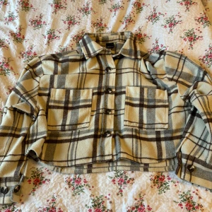 Jacka - Säljer en beige och brun rutig jacka. Den har en croppad passform med knappar framtill och två stora bröstfickor. Perfekt för lager-på-lager-stil!