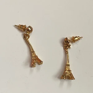 Guldörhängen med Eiffeltornet - Charmiga guldörhängen formade som Eiffeltornet. Perfekta för att ge en touch av Parisisk elegans till din stil. De är små och lätta, vilket gör dem bekväma att bära hela dagen.