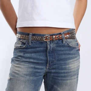 Brunt bälte med nitar - Snyggt brunt bälte med silverfärgade nitar som ger en cool look. Perfekt för att ge extra edge till din outfit. Passar bra till jeans och andra casual kläder.