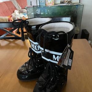 Svarta Moon Boots med snörning - Snygga svarta Moon Boots i syntetmaterial med vit logga och snörning. Så HIMLA SKÖNA men dom har aldrig kommit till användning. Prislappen sitter kvar och dom är i helt nyskick💕