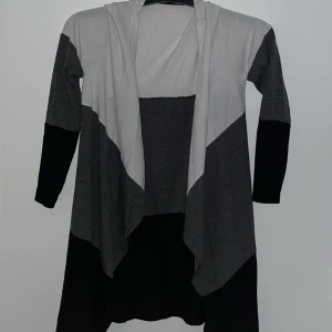 Svart och grå kofta - Säljer en stilren svart och grå kofta med långa ärmar. Perfekt för lager-på-lager och passar till många olika outfits. Koftan har en öppen design utan knappar.