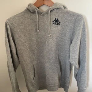 Grå hoodie från Kappa - Säljer en grå hoodie från Kappa med logga både fram och bak. Köpt på plick men ändå bra skick utan defekter 