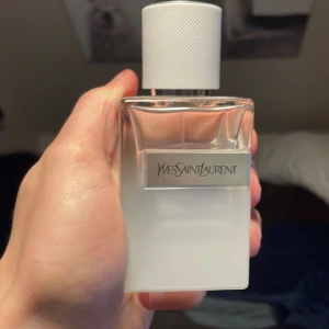 Parfym från Yves Saint Laurent - Säljer en elegant parfym från Yves Saint Laurent. Flaskan är fyrkantig med en frostad glasdesign och har en vit kork med YSL-logotypen på toppen. Den stilrena metallplattan på framsidan ger en lyxig känsla. Perfekt för den som vill ha en sofistikerad doft.    Villig att sälja för 650