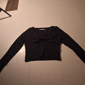 Svart ribbad topp från Abercrombie & Fitch - Snygg svart ribbad topp från Abercrombie & Fitch med långa ärmar och en knytning framtill. Perfekt för en stilren look.