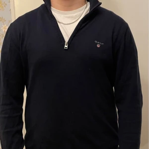 Svart tröja med dragkedja från Gant - Snygg mörkblå tröja från Gant med halv dragkedja och diskret logga på bröstet. Perfekt för en stilren look.