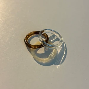 Tre stilrena ringar i akryl - Säljer två stilrena ringar i akryl, en i klar transparent och en i brun nyans. Perfekta för att addera en modern touch till din look. De är lätta och bekväma att bära.