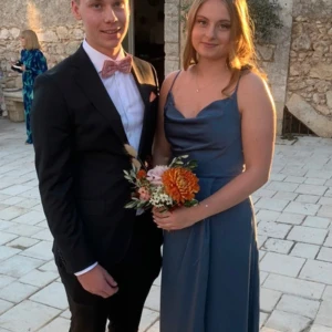 Blå långklänning -  blå långklänning med smala axelband och en vacker drapering över bysten. Klänningen har en figurnära passform som framhäver midjan och ger en stilren siluett. Perfekt för festliga tillfällen tex bal .