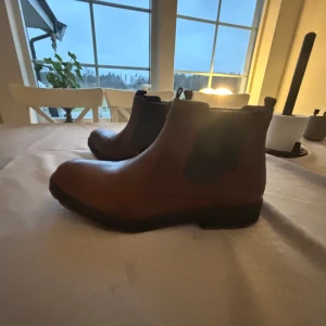 Bruna , Fodrade Chelsea boots - Snygga bruna Chelsea boots i skinn med elastiska paneler på sidorna för enkel på- och avtagning. Perfekta för både höst, vår  och vinter med en robust sula för bra grepp, lätt fodring som håller fötterna varma. Jobbbara skor. Helt oanvända, köpta för ca 4 månader sen 