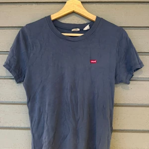 Blå t-shirt från Levi's - Blå t-shirt från Levi's med deras ikoniska röda logga på bröstet. T-shirten har en klassisk rund hals och korta ärmar. 