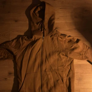 Brun hoodie från Jack & Jones - Säljer en brun hoodie från Jack & Jones med dragkedja och huva. Perfekt för en avslappnad stil. Den har långa ärmar och en bekväm passform.