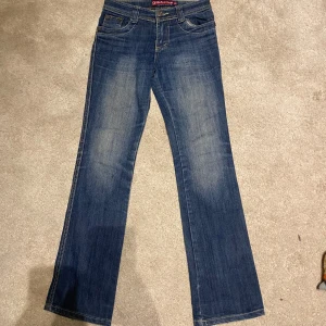 Blå jeans från DikeWang - Snygga blå jeans från DikeWang med design på bakfickorna. De har en bootcut-stil och Midjan är lowwaist och de har en knapp och dragkedja framtill. Midjemått 35cm rakt över och internens längd 76cm. Skriv för mer frågor eller bilder!