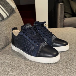 Christian Louboutin Navy Blue Leather and Suede Louis Junior Sneakers - Snygga blå sneakers från Christian Louboutin med klassisk röd sula och snörning. Skorna har en kombination av skinn och meshmaterial för en modern look. Otroligt bra skick, endast skorna medföljer vid köp. Givetvis äkta! Hör av dig vid minsta fundering!