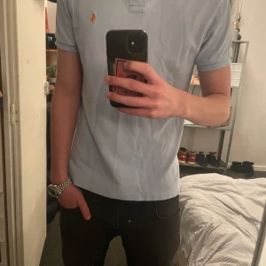 Ljusblå pikétröja från Ralph Lauren - Säljer en stilren ljusblå pikétröja från Ralph Lauren med klassisk krage och knappar. Tröjan har ett orange märke och är i fint skick. Hör av dig för frågor! 🚀