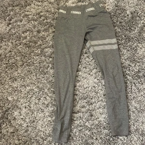 Grå leggings från Stronger - Snygga grå leggings från Stronger med elastisk midja och textdetaljer. Perfekta för träning med en bekväm passform och stilrena mönster på benet.