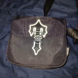 Svart axelväska från Trapstar - Tar bara kontant möts i Eskilstuna Örebro Arboga.Snygg svart axelväska från Trapstar med ett unikt spänne framtill. Väskan har en justerbar axelrem med märkets logga tryckt på. Perfekt för att bära dina viktigaste saker med stil.