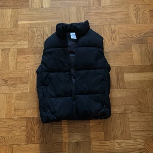 Svart dunväst från Zara - Säljer en stilren svart dunväst från Zara. Västen har en dragkedja framtill och är quiltad för extra värme. Perfekt för kyligare dagar och lätt att matcha med olika outfits.