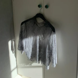 Grå spetsblus från Ganni - Säljer en grå spetsblus från Ganni. Blusen har långa ärmar och ett vackert spetsmönster. Perfekt som en cool blus att lägga till i festgarderoben. Tar absolut emot bud💋