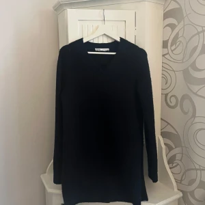 Svart tröja från Zara - Säljer en stilren svart stickad klänning från Zara med v-ringning. Klänningen har långa ärmar och är perfekt för kyligare dagar. Enkel och klassisk design som passar till det mesta.