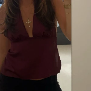 Vinröd halterneck topp från Gina  - Snygg vinröd halterneck topp med knytning i ryggen. Perfekt för en kväll ute eller en somrig dag. Toppen har en djup v-ringning och är ärmlös, vilket ger en elegant och luftig känsla.