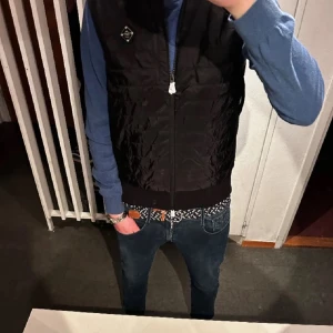 Svart quiltad väst från J. Lindeberg - Snygg svart quiltad väst från J. Lindeberg med dragkedja framtill. Perfekt för lager-på-lager-stil och håller dig varm under kalla dagar.