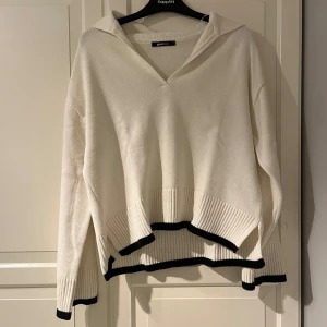 Vit stickad tröja med svarta detaljer - Snygg vit stickad tröja från Gina Tricot med svarta ribbade kanter. Tröjan har en v-ringad krage och långa ärmar. Skönt material