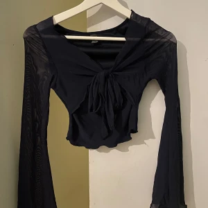 Marinblå transparent topp med knyt - Snygg marinblå topp med långa transparenta ärmar och knyt framtill. Perfekt för en kväll ute eller en speciell tillställning. Toppen har en croppad passform och är tillverkad i ett lätt och luftigt material.