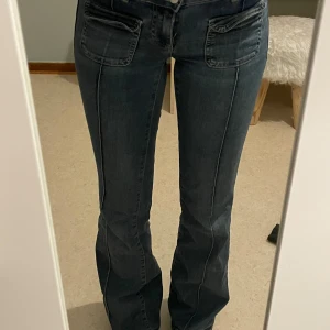 Blå bootcut jeans - Snygga blå bootcut jeans med låg midja och dubbla knappar fram. Köpte på Nelly för ett tag sen, men har bara använt ett par gånger så att de är i fint skick dock är de lite slitage på sömmarna längst ner. Fickorna kan behöva strykas lite. 