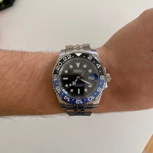 Seiko Batman/Batgirl GMT-Master II Mod - Kom med bud, helt ny! Säljer en Seiko klocka med en stilren design. Den har en blå och svart bezel med 24-timmarsmarkeringar och en svart urtavla med lysande visare och index. Armbandet är i silverfärgat stål med en säkerhetslåsning. Perfekt för den som gillar en klassisk och funktionell stil.