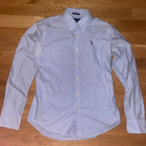 Ralph Lauren skjorta - Snygg ljusblå skjorta från Ralph Lauren i slim fit. Tillverkad i 100% bomull med klassisk krage och broderad logotyp på bröstet. Perfekt för en stilren look. Storleken motsvarar XS