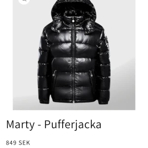 Svart pufferjacka från Marty - Snygg glansig svart pufferjacka från Marty med huva och dragkedja. Jackan är helt ny med lappar, endast provad. Säljer pga fel storlek och returfrakt med tull blev för dyrt. Mitt pris 600 kr. 