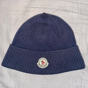 Blå stickad mössa från Moncler - Snygg blå stickad mössa från Moncler med uppvikt kant och broderad logotyp framtill. Perfekt för kyliga dagar.