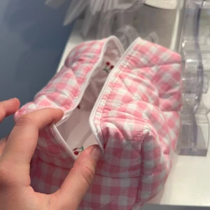 Rutig rosa necessär - Söt liten necessär i rosa och vitt rutigt mönster med dragkedja. Insidan har ett charmigt körsbärsmönster. Perfekt för att förvara smink eller småsaker. Handgjord 