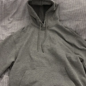 Grå hoodie från Pull&Bear - Säljer en stilren grå hoodie från Pull&Bear. Den har en klassisk design med en stor ficka framtill och justerbar huva med dragsko. Perfekt för en avslappnad look.