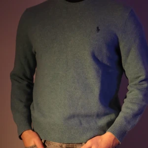 Grön/blå tröja från Ralph Lauren - Säljer en stilren grön/blå tröja från Ralph Lauren med broderad logga på bröstet. Tröjan har långa ärmar och ribbade muddar vid ärmslut och nederkant. Perfekt för en klassisk look. 