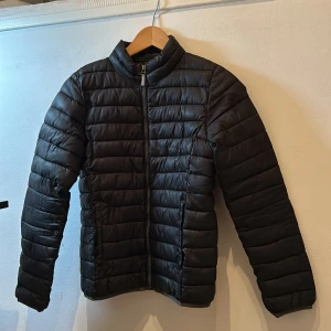 Svart dunjacka från Mywear Active - Säljer en svart dunjacka från Mywear Active. Jackan har en dragkedja framtill och är quiltad för extra värme. Perfekt för kyligare dagar med sin långa ärmar och stilrena design.