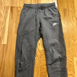 Grå mjukisbyxor från Nike - Säljer ett par grå mjukisbyxor från Nike med elastisk midja och logga på benet. Perfekta för en avslappnad stil eller träning.