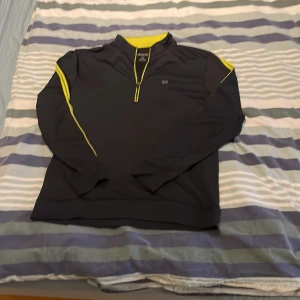 Svart tröja med gula detaljer från Calvin Klein - Snygg svart tröja från Calvin Klein med gula detaljer längs ärmarna och dragkedja. Perfekt för en sportig look. Tröjan har en liten CK-logga på bröstet och baksidan. Pris går alltid att förhandlas.